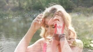 A blonde girl caresses herself on the shores of a lake